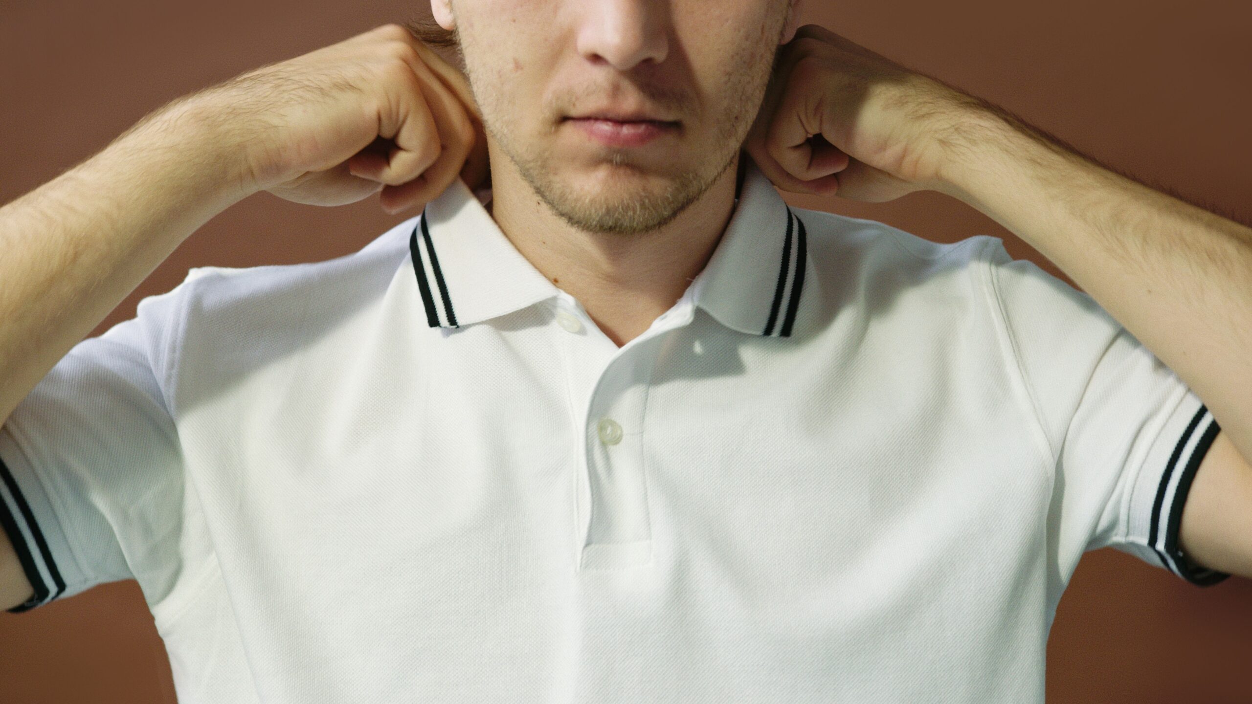 pexels photo 7648278 7648278 1 Close-up portrait of a man adjusting his polo shirt collar, artistic lighting.